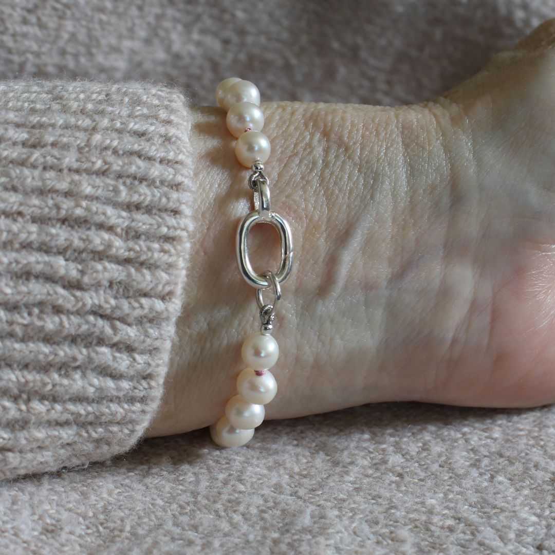 A close-up of a person's wrist wearing a pearl and silver bracelet, styled with a beige knit sweater cuff.