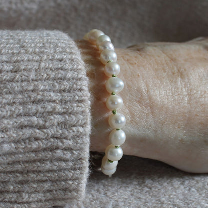 A close-up of a white pearl
bracelet worn on a person's wrist, paired with a textured light gray knit sweater cuff.