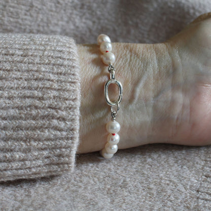 A close-up of a pearl  bracelet with a silver clasp worn on a wrist, paired with a beige knit sweater cuff.