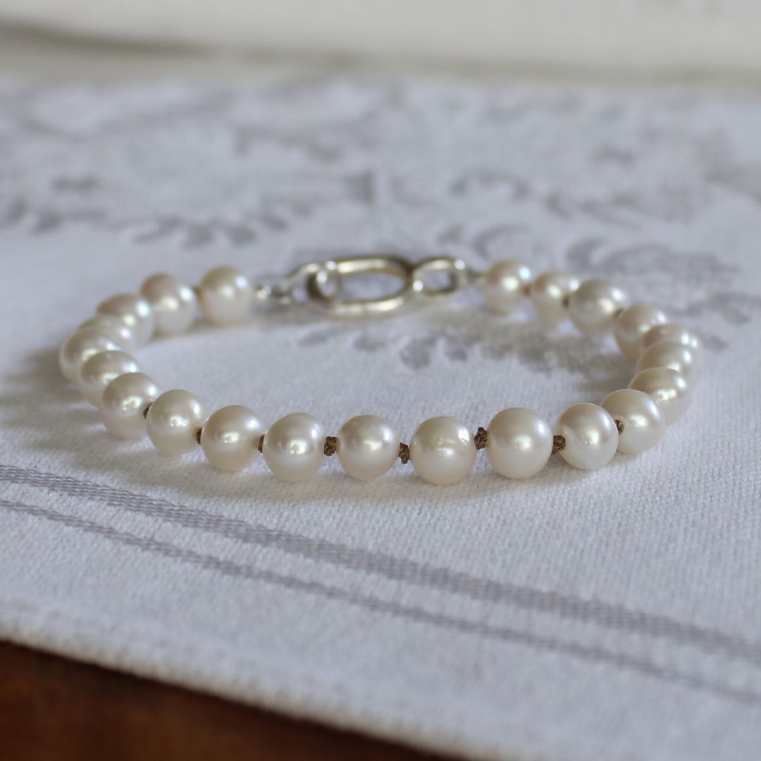A pearl beaded bracelet with a silver clasp resting on a white patterned fabric surface.