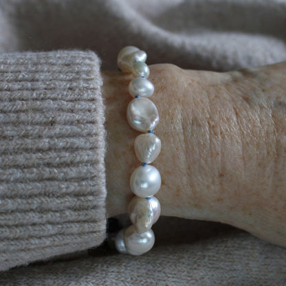 A close-up of a person's wrist wearing a mixed pearl bracelet hand-knotted on delft silk, paired with a beige ribbed knit sweater cuff.