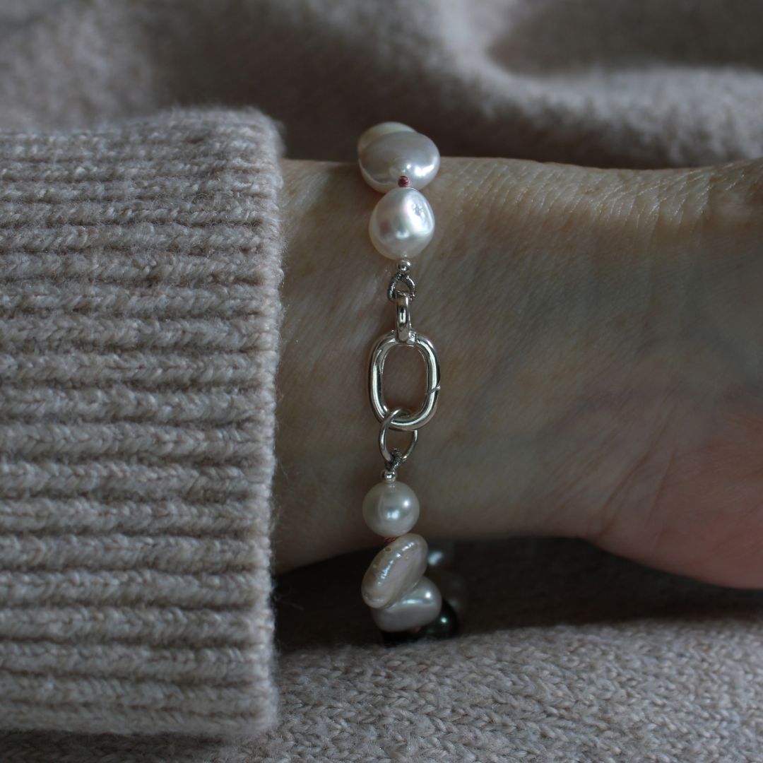 A mixed pearl bracelet made of keshi, round, baroque, peacock pearls hand-knotted on old rose silk, worn on a wrist covered by a beige ribbed knit cuff.