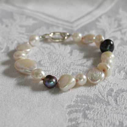 A mixed pearl bracelet made of keshi, round, baroque, peacock pearls hand-knotted on old rose silk, displayed on a textured white fabric background.