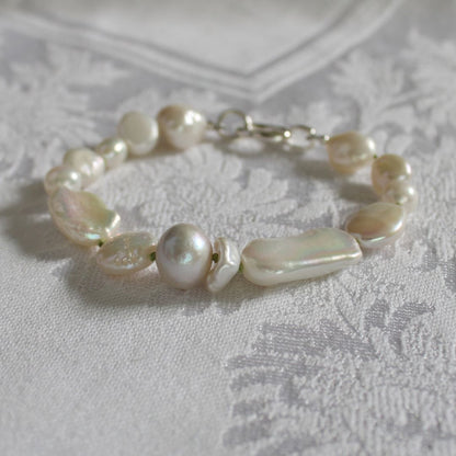 A mixed pearl bracelet hand-knotted on peridot silk with a silver clasp, resting on a white textured lace fabric background.