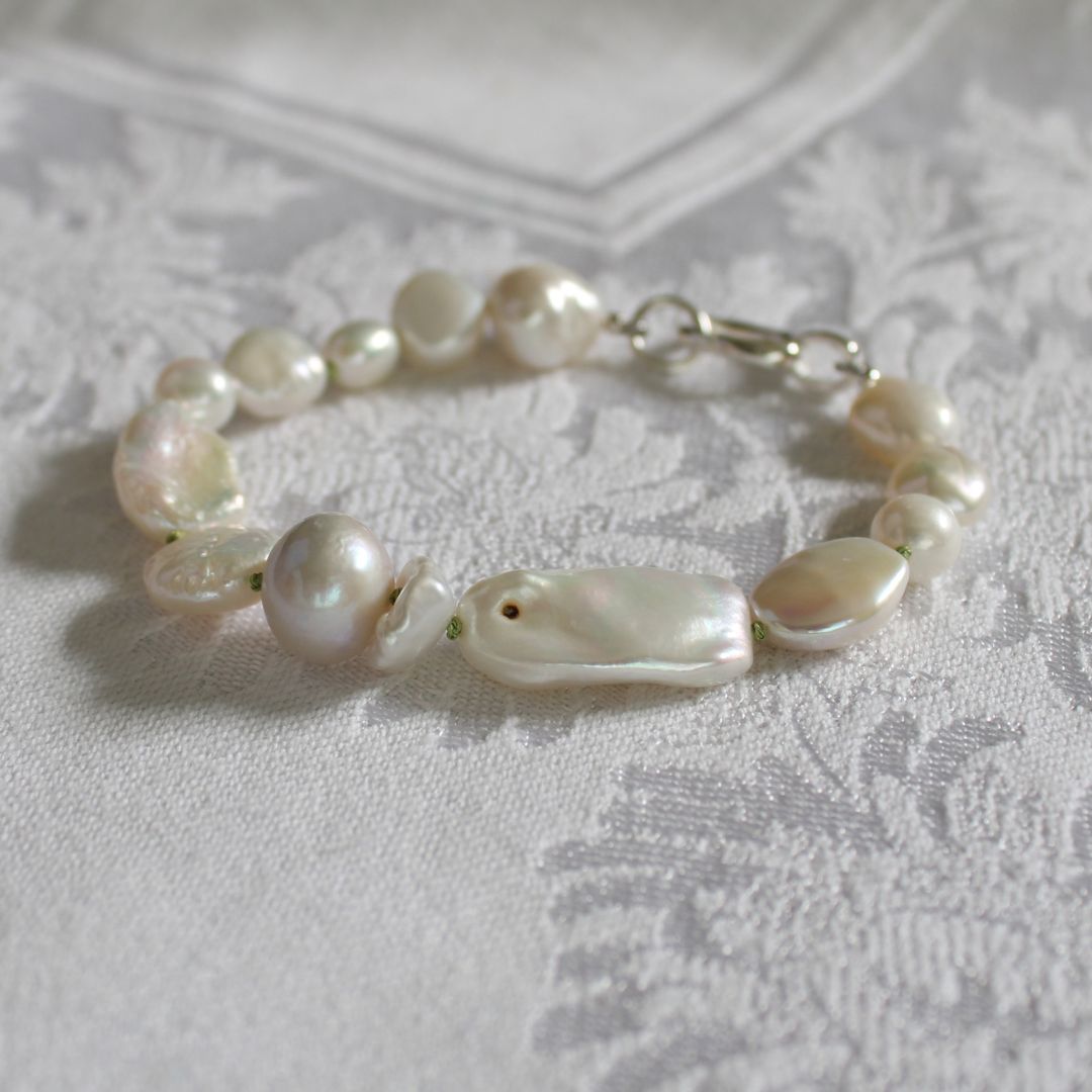 A mixed pearl bracelet with a silver clasp, showing a blemish on a large pearl, resting on a textured white damask fabric background.