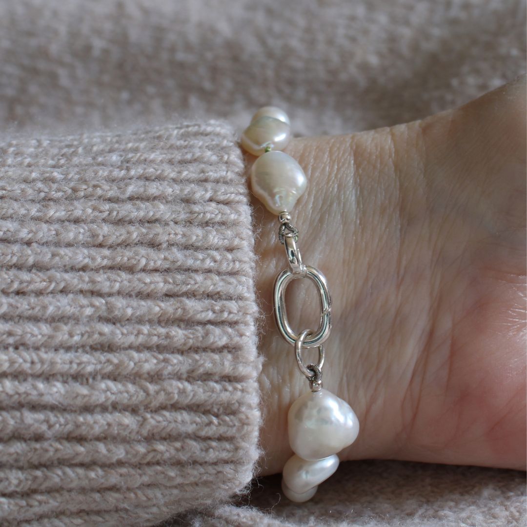 A close up of a mixed pearl bracelet showing the easy close sterling silver clasp, on wrist with beige cuff.