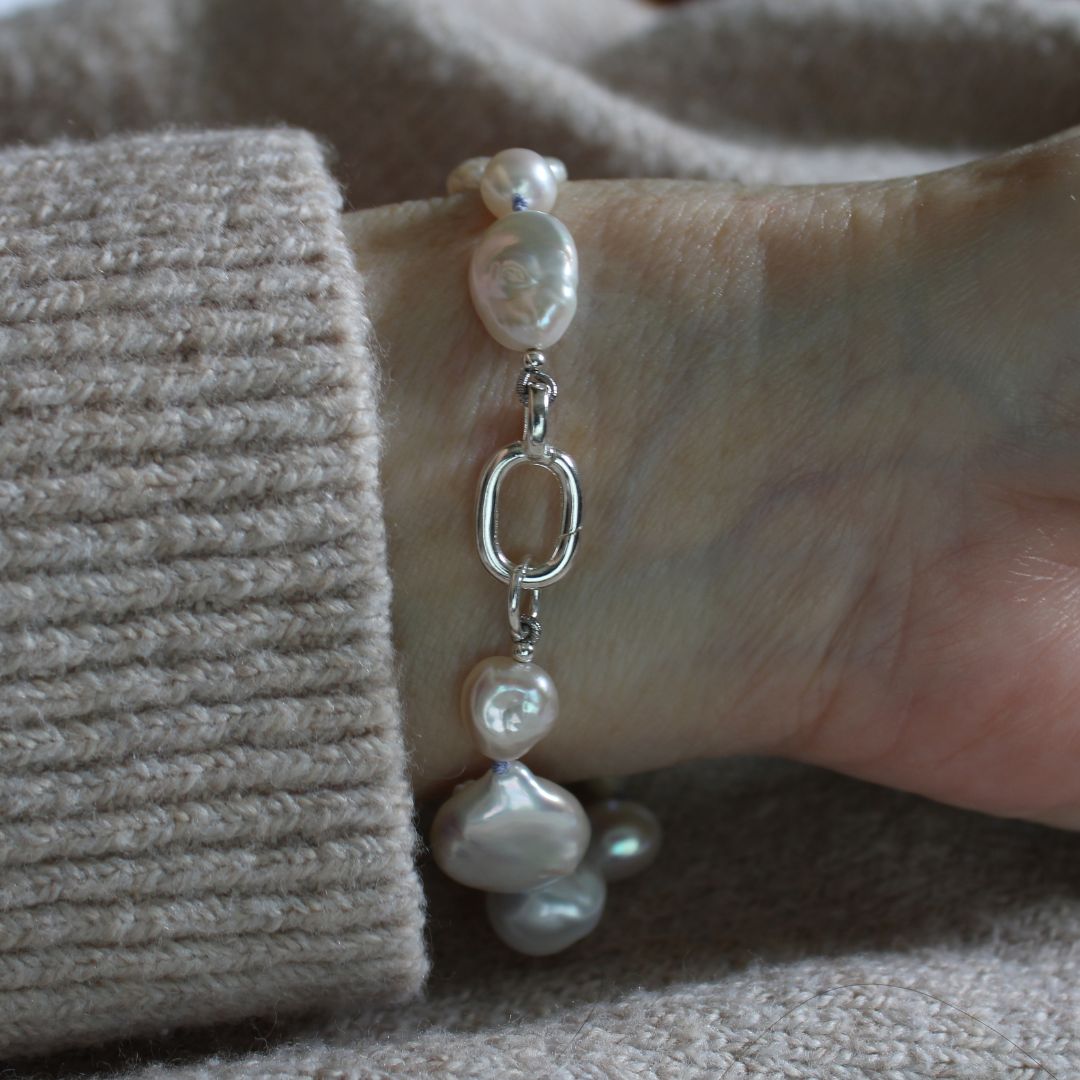 A close-up of a person's wrist wearing a mixed pearl bracelet showing the sterling silver easy close charmer clasp, styled with a beige ribbed knit sweater cuff.