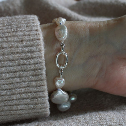 A close-up of a person's wrist wearing a mixed pearl bracelet showing the sterling silver easy close charmer clasp, styled with a beige ribbed knit sweater cuff.