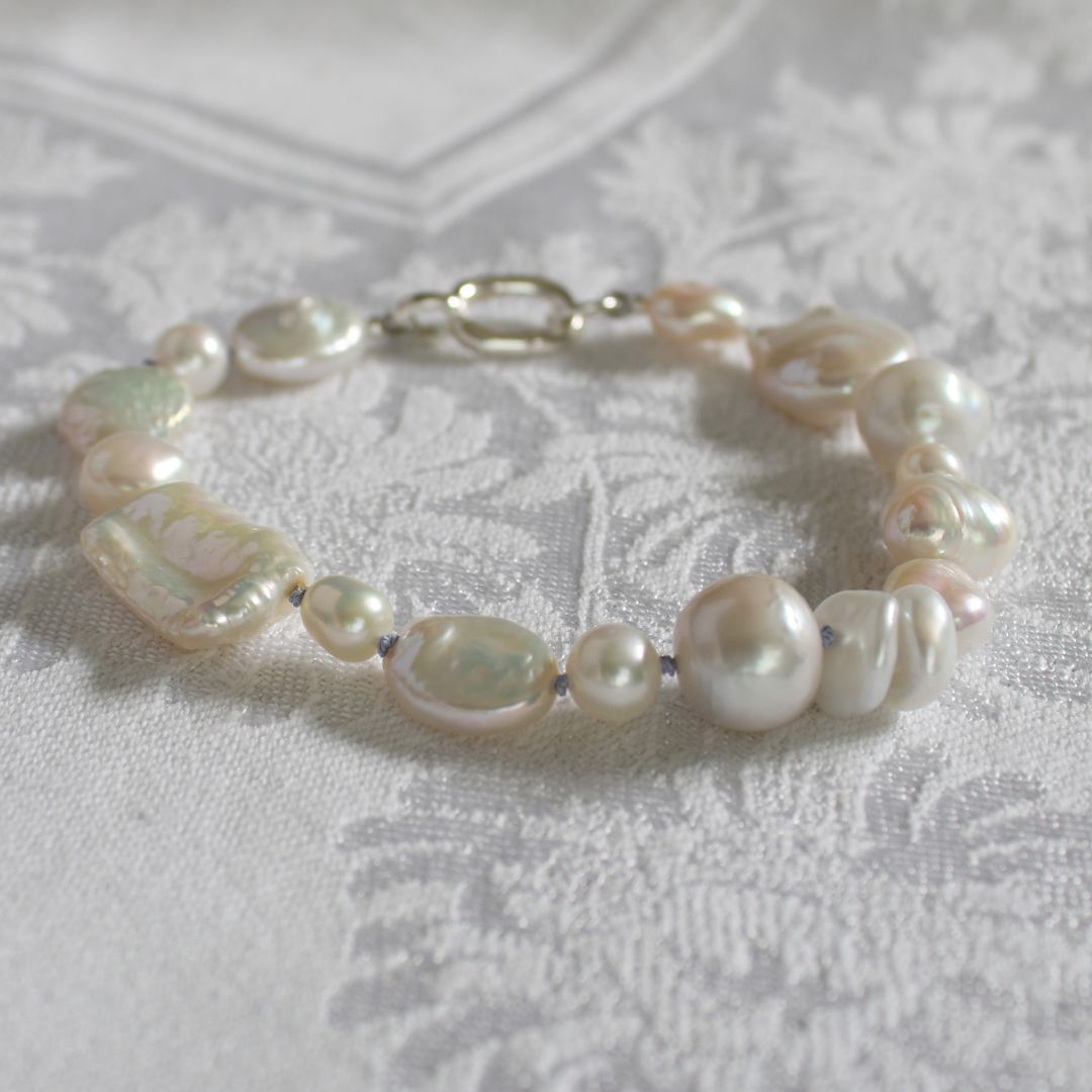 A hand-knotted mixed pearl bracelet with a silver clasp, resting on a textured white damask fabric.