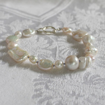 A hand-knotted mixed pearl bracelet with a silver clasp, resting on a textured white damask fabric.