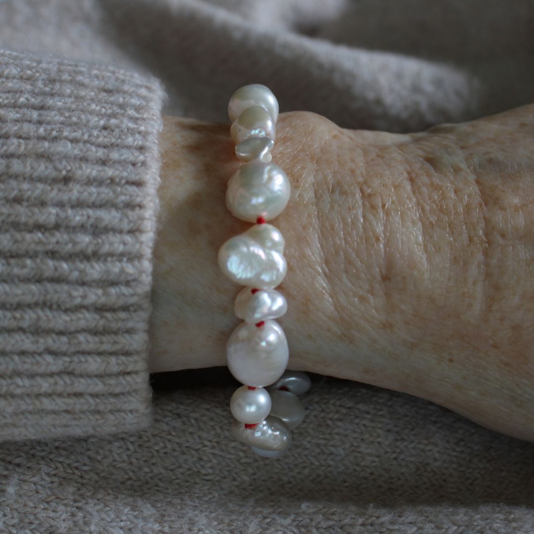 A close-up of a person's wrist wearing a hand-knotted mixed pearl bracelet, worn over a beige knit sweater.