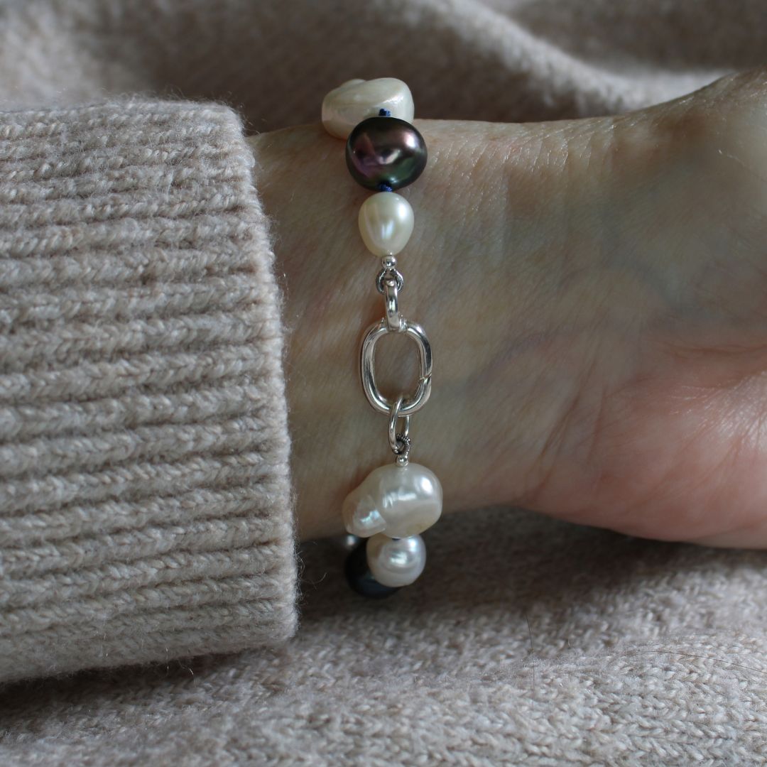A close-up of a person's wrist wearing a mixed pearl bracelet made of keshi, round, baroque, peacock pearls hand-knotted on sapphire silk, showing the sterling silver easy close charmer clasp.