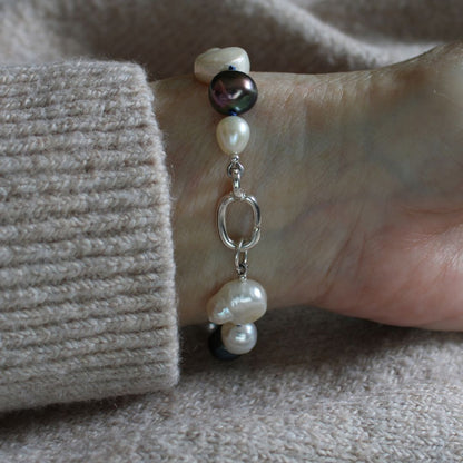 A close-up of a person's wrist wearing a mixed pearl bracelet made of keshi, round, baroque, peacock pearls hand-knotted on sapphire silk, showing the sterling silver easy close charmer clasp.