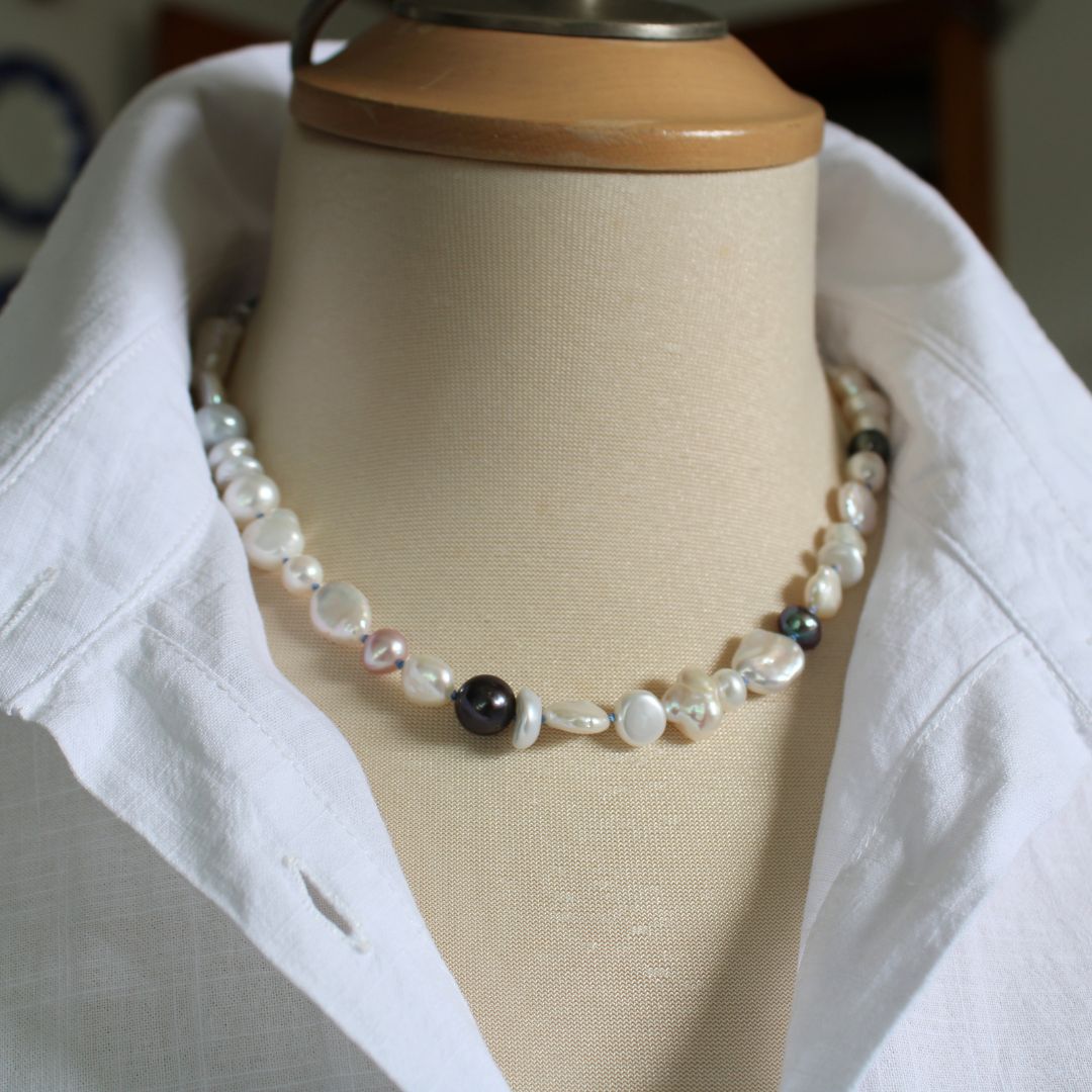 One-of-a-kind mixed pearl necklace with keshi, coin, round, baroque, and peacock pearls hand-knotted on delft silk, shown on mannequin with white linen blouse with stand-up collar.