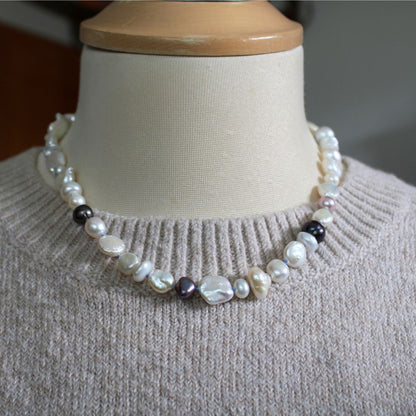 One-of-a-kind mixed pearl necklace with keshi, coin, round, baroque, and peacock pearls hand-knotted on delft silk, shown on mannequin with beige knitted sweater.