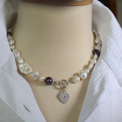 One-of-a-kind mixed pearl necklace with keshi, coin, round, baroque, and peacock pearls hand-knotted on delft silk, and showing 13mm sterling silver round charmer clasp and sterling silver  hand-stamped initial heart charm, shown on mannequin with white linen blouse and stand up collar.