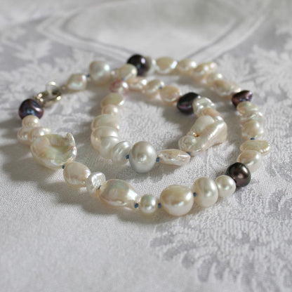One-of-a-kind mixed pearl necklace with keshi, coin, round, baroque, and peacock pearls hand-knotted on delft silk, laying on a linen cloth.