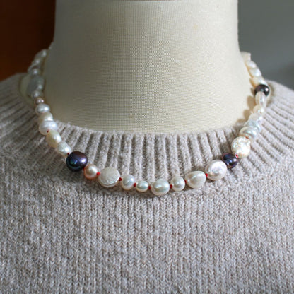 One-of-a-kind mixed pearl necklace with keshi, coin, round, baroque, and peacock pearls hand-knotted on ruby silk, shown on mannequin with beige knitted sweater.