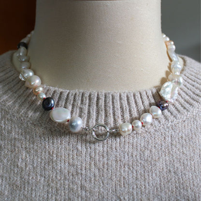 One-of-a-kind mixed pearl necklace with keshi, coin, round, baroque, and peacock pearls hand-knotted on ruby silk, and showing 13mm sterling silver round charmer clasp, shown on mannequin with beige knitted sweater.