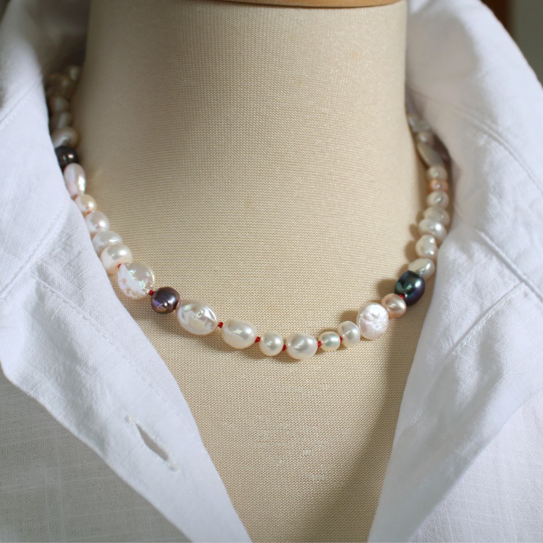 One-of-a-kind mixed pearl necklace with keshi, coin, round, baroque, and peacock pearls hand-knotted on ruby silk, shown on mannequin with white linen blouse with upturned collar.