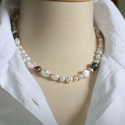 One-of-a-kind mixed pearl necklace with keshi, coin, round, baroque, and peacock pearls hand-knotted on ruby silk, shown on mannequin with white linen blouse with upturned collar.