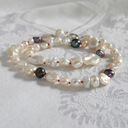 One-of-a-kind mixed pearl necklace with keshi, coin, round, baroque, and peacock pearls hand-knotted on ruby silk, laying on a linen cloth. 
