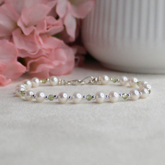 Pearl bracelet with peridot gemstones and sterling silver beads on a light surface with pink flowers in the background
